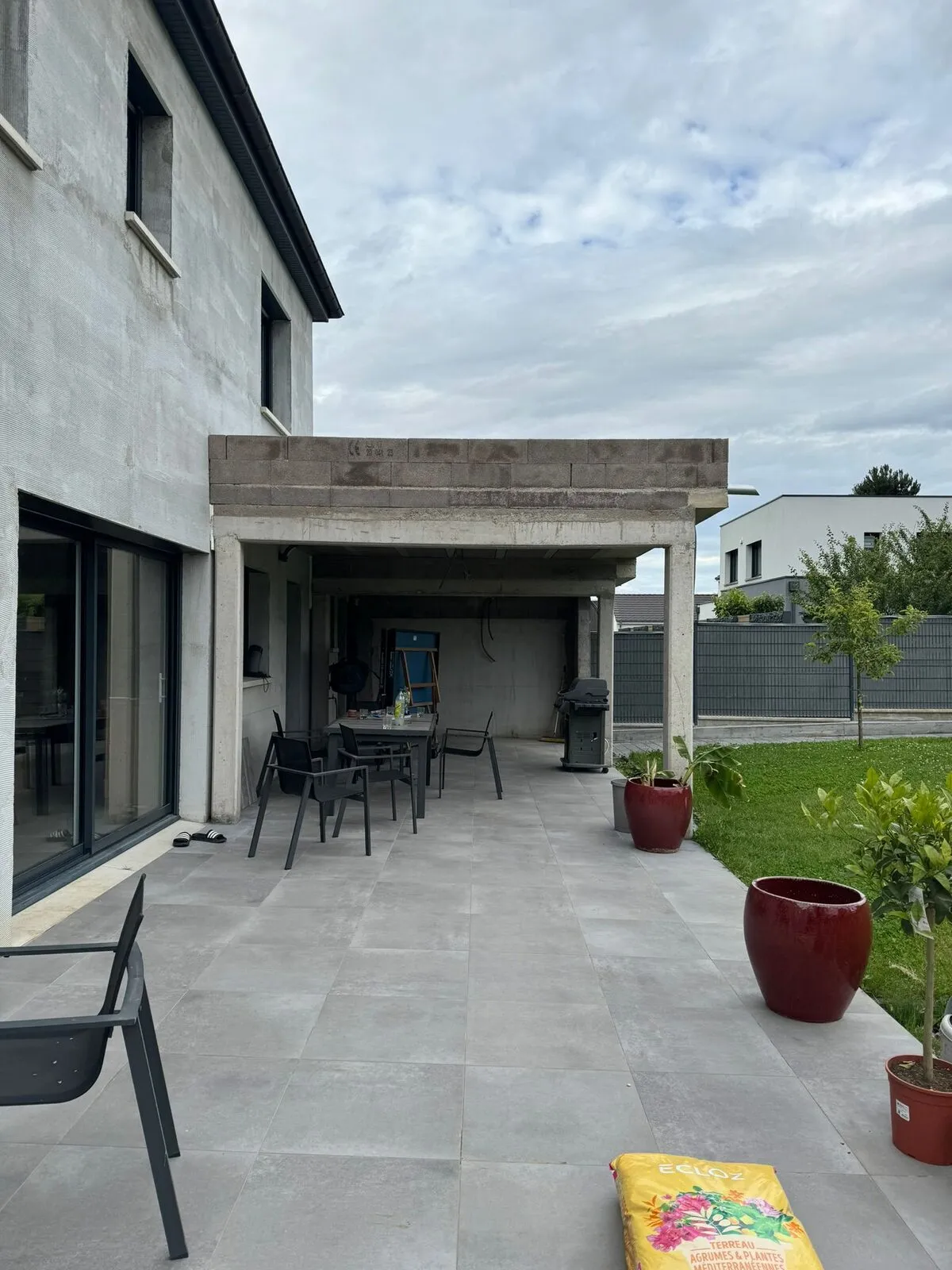 Terrasse en dalles grises et extension avec auvent béton d'une maison moderne, réalisées près de Metz